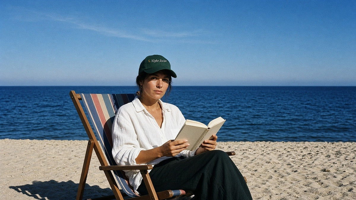 The Night Swim Dad Hat in Spruce, worn by a woman reading in a striped deck chair