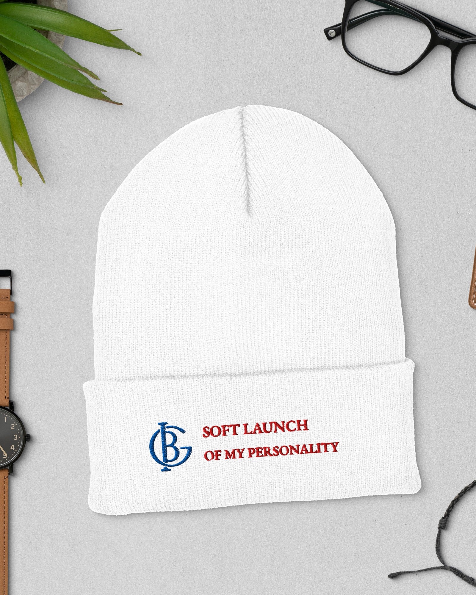 The Soft Launch Beanie in White, flat lay with a watch and glasses
