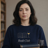 The Book Club Crewneck in Navy, worn in a library aisle with a stack of books and a glass of wine