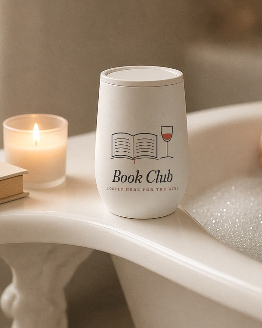 The Book Club Wine Tumbler on the edge of a bathtub with a candle and a book