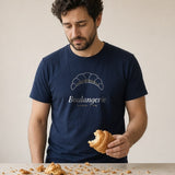 The Boulangerie Tee in True Navy, a man at a café counter, flakes of croissant all over his True Navy tee, looking down at them with mild concern