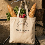 The Boulangerie Tote in Oyster, two baguettes and a bunch of radishes sticking out of the tote, on a bike rack outside a bakery