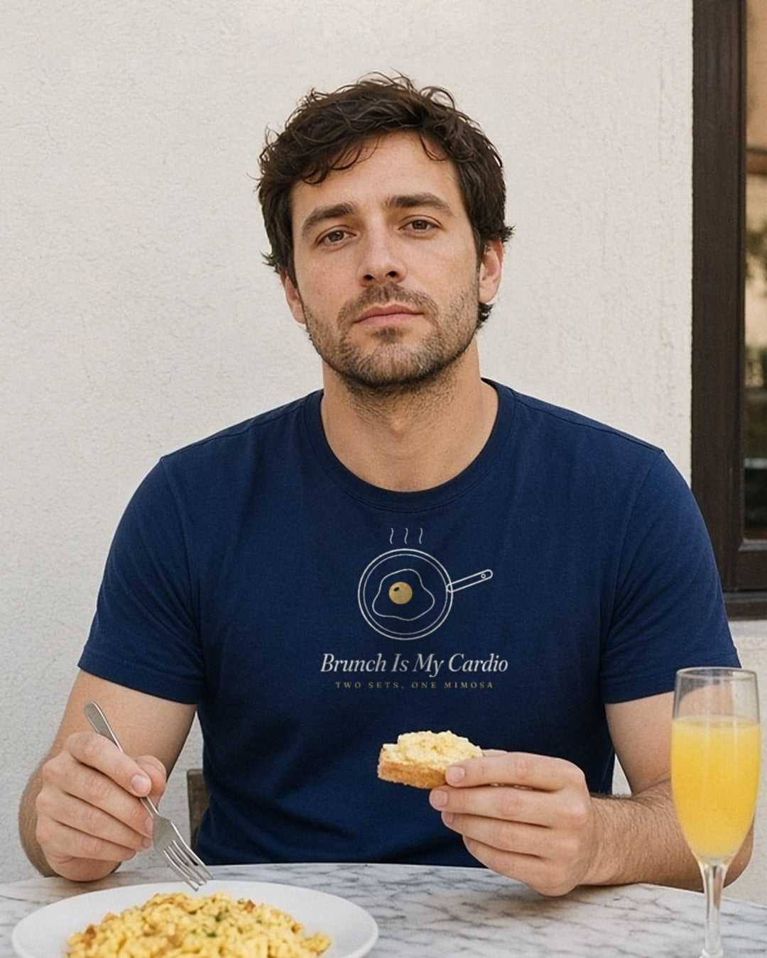 The Brunch Is My Cardio Tee in True Navy, man at a sunny breakfast table with scrambled eggs, toast and a mimosa