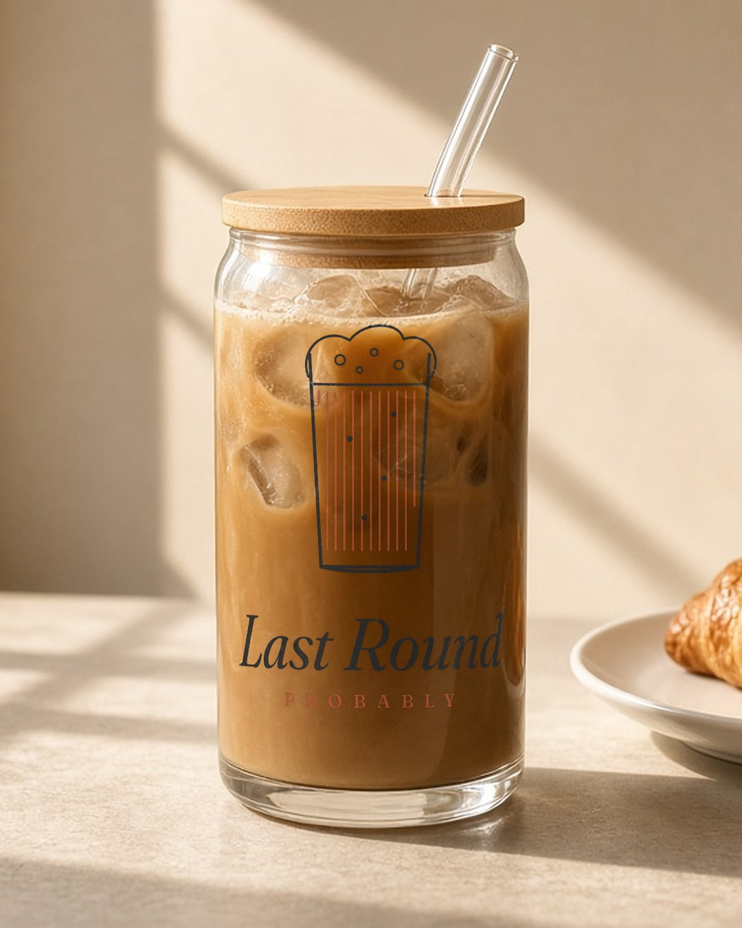 The Last Round Can Glass in Clear 16 oz, iced coffee with a bamboo lid and glass straw on a sunny counter