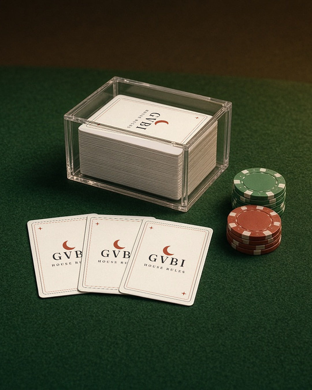 The House Rules Playing Cards, three cards on green felt beside the deck in its clear box and a stack of poker chips