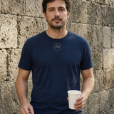 The House Crest Tee in True Navy, man against an old stone wall holding a coffee cup and keys