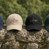 The House Dad Hat in Navy, Stone, Black, Spruce, all four colours on a stone wall, greenery behind