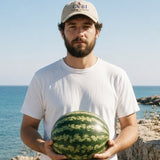 The House Dad Hat in Stone, man by the sea holding a watermelon in both hands