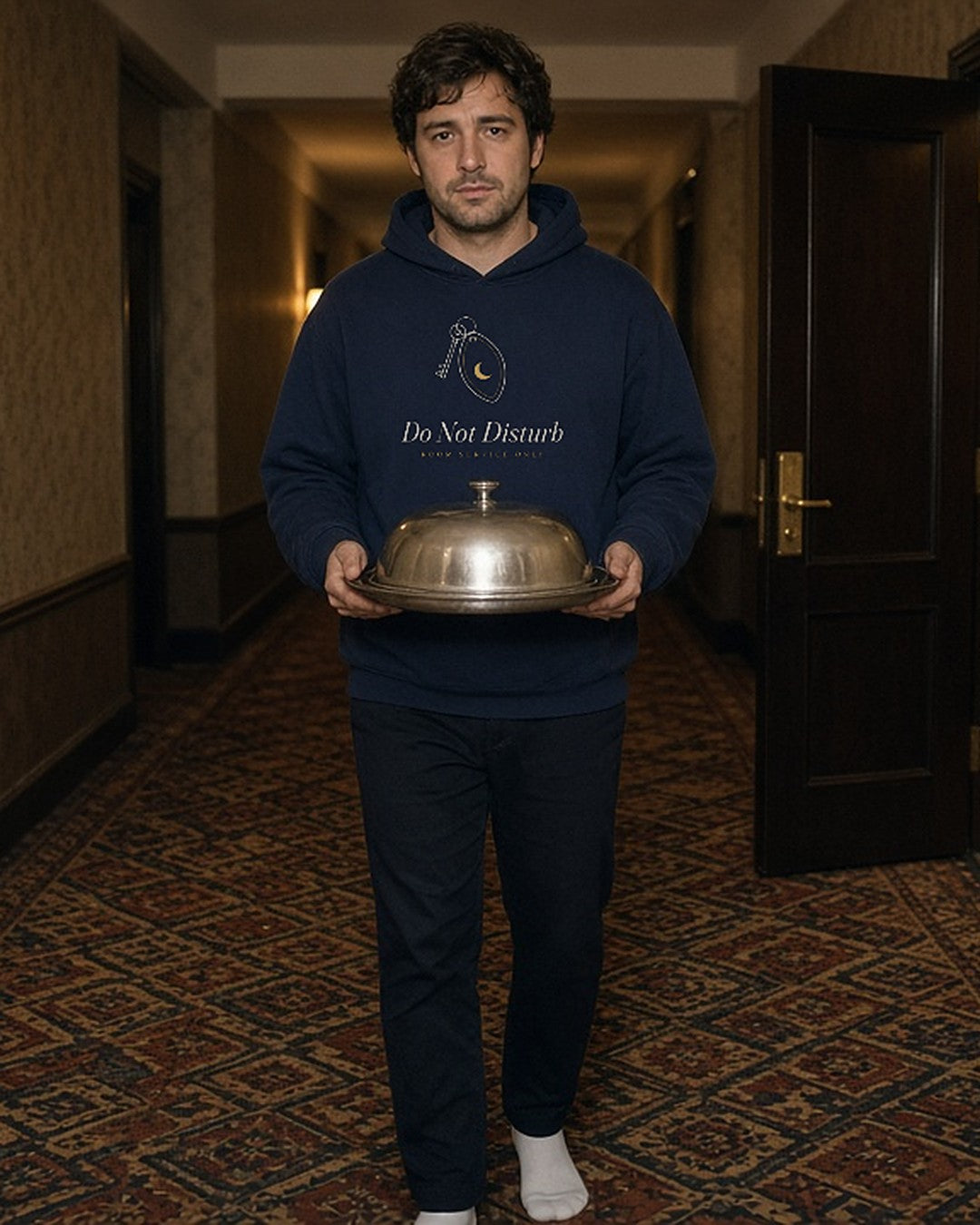 The Do Not Disturb Hoodie in Navy Blazer, worn in a hotel hallway with a room-service cloche