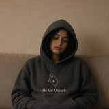 The Do Not Disturb Hoodie in Charcoal Heather, worn hood up by a woman asleep sitting up on a long couch