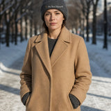 The Do Not Disturb Beanie in Dark Grey, woman in a camel coat on a snowy tree-lined path