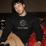 The Early Night Crewneck in Black, young man in the Black crew asleep sitting up on a pile of party coats on a bed (coats run off both sides)