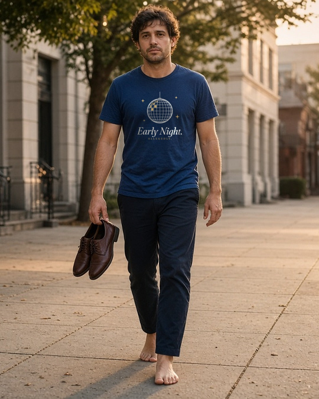 The Early Night Tee in True Navy, a man (30s) in True Navy walking home at sunrise carrying his shoes