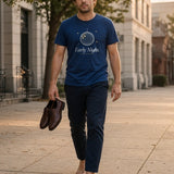 The Early Night Tee in True Navy, a man (30s) in True Navy walking home at sunrise carrying his shoes
