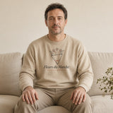 The Fleurs du Marché Crewneck in Sand, a man in Sand on a sofa with a full vase on the coffee table and nowhere to be
