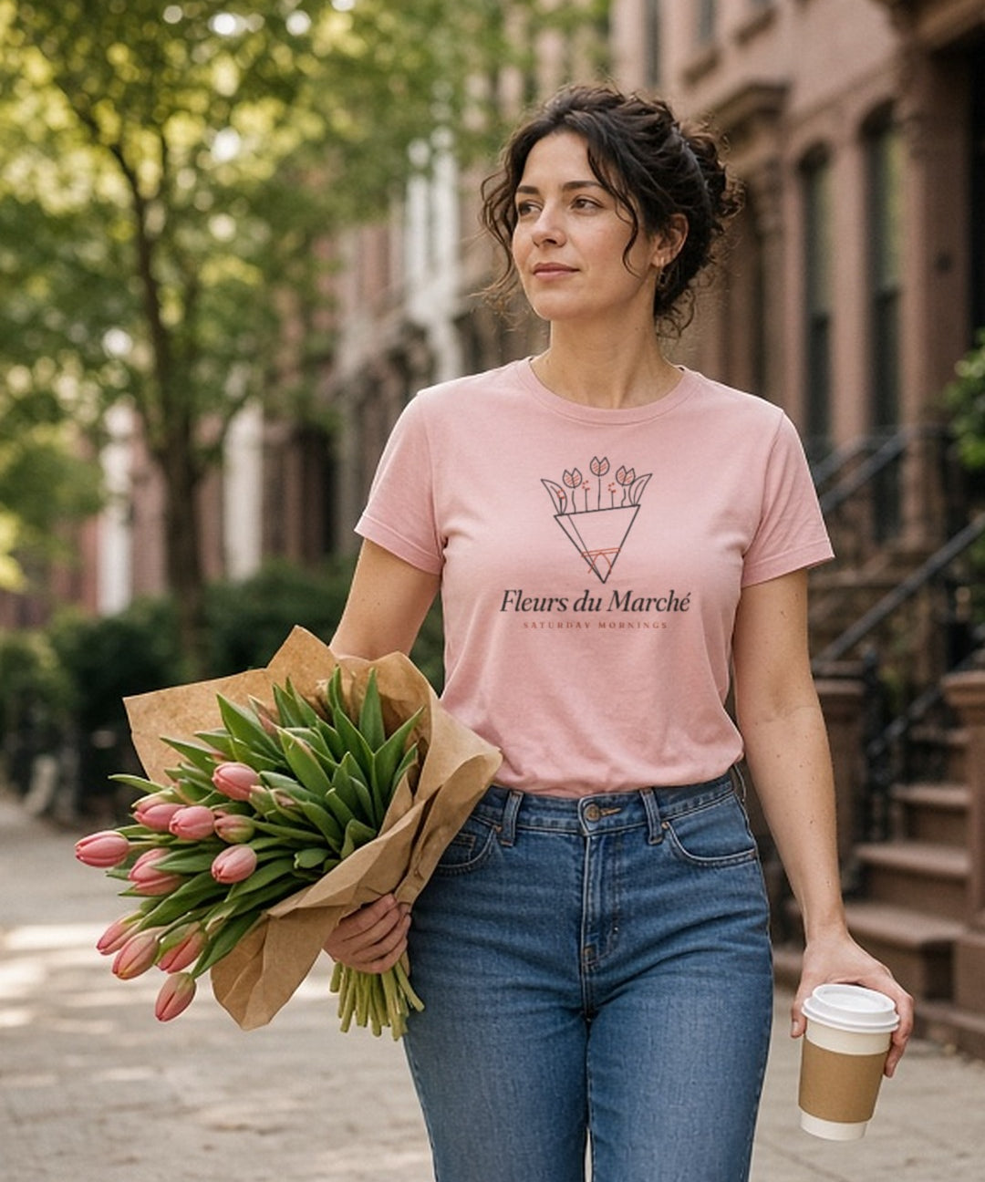 The Fleurs du Marché Tee in Blossom, a woman (30s) walks home with an armful of tulips far too big for her, coffee balanced on top, Blossom tee