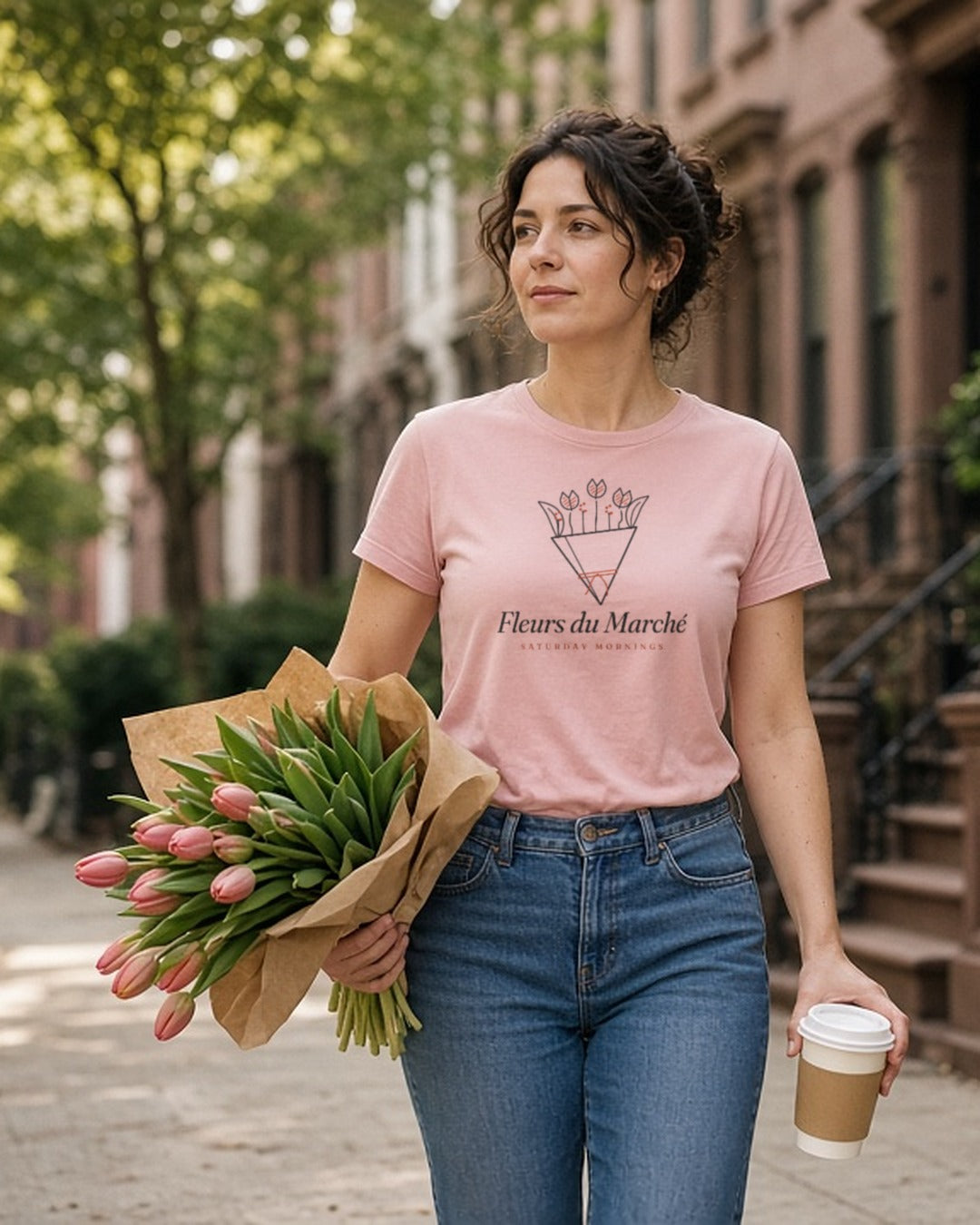 The Fleurs du Marché Tee in Blossom, a woman (30s) walks home with an armful of tulips far too big for her, coffee balanced on top, Blossom tee
