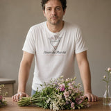 The Fleurs du Marché Tee in White, a man (40s) in the White tee stares at three bouquets and one tiny vase on a kitchen table