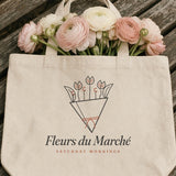 The Fleurs du Marché Tote in Oyster, the tote on a wooden bench with a bunch of ranunculus lying across the top edge