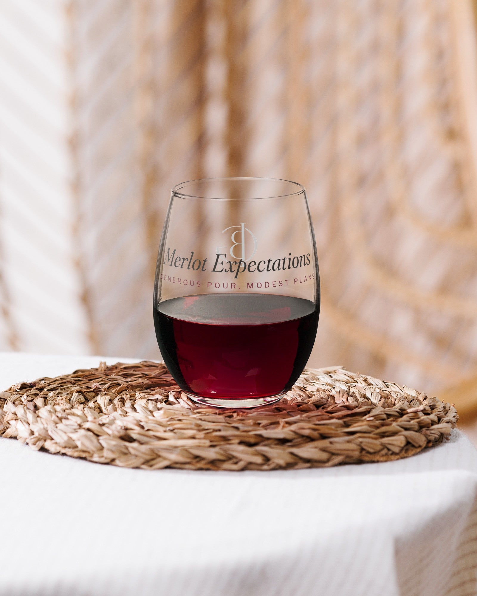 The Merlot Expectations Wine Glass with red wine on a woven placemat