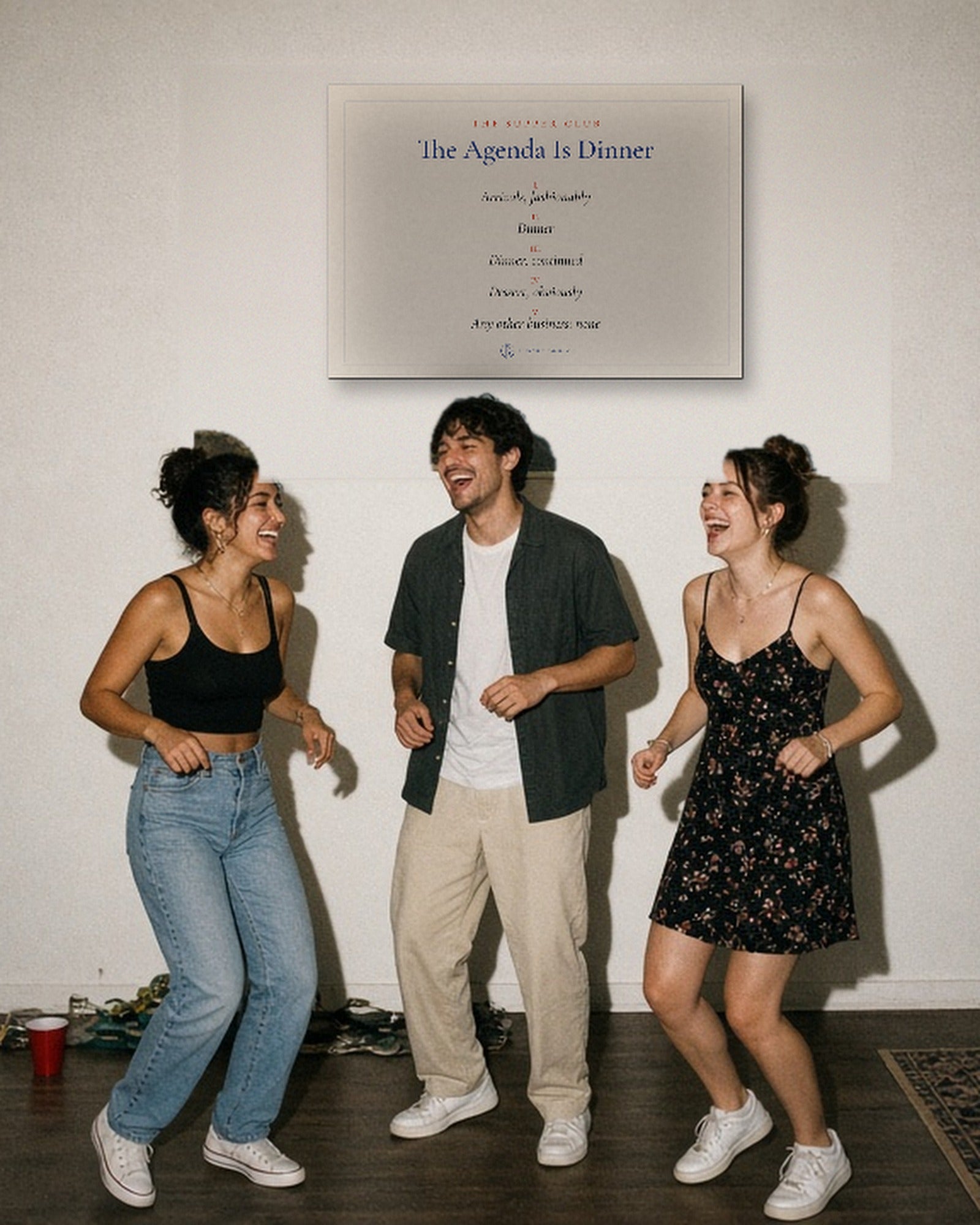 Three friends dancing at a house party under The Agenda Is Dinner Print hanging on a white wall