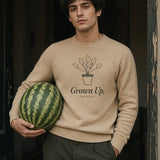 The Grown Up, Mostly Crewneck in Sand, holding a whole watermelon in a doorway