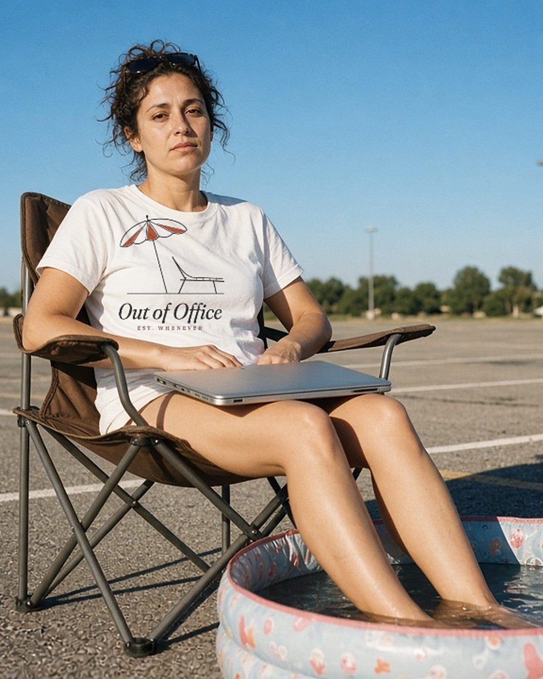 The Out of Office Tee in White, feet in a kiddie pool in an empty parking lot