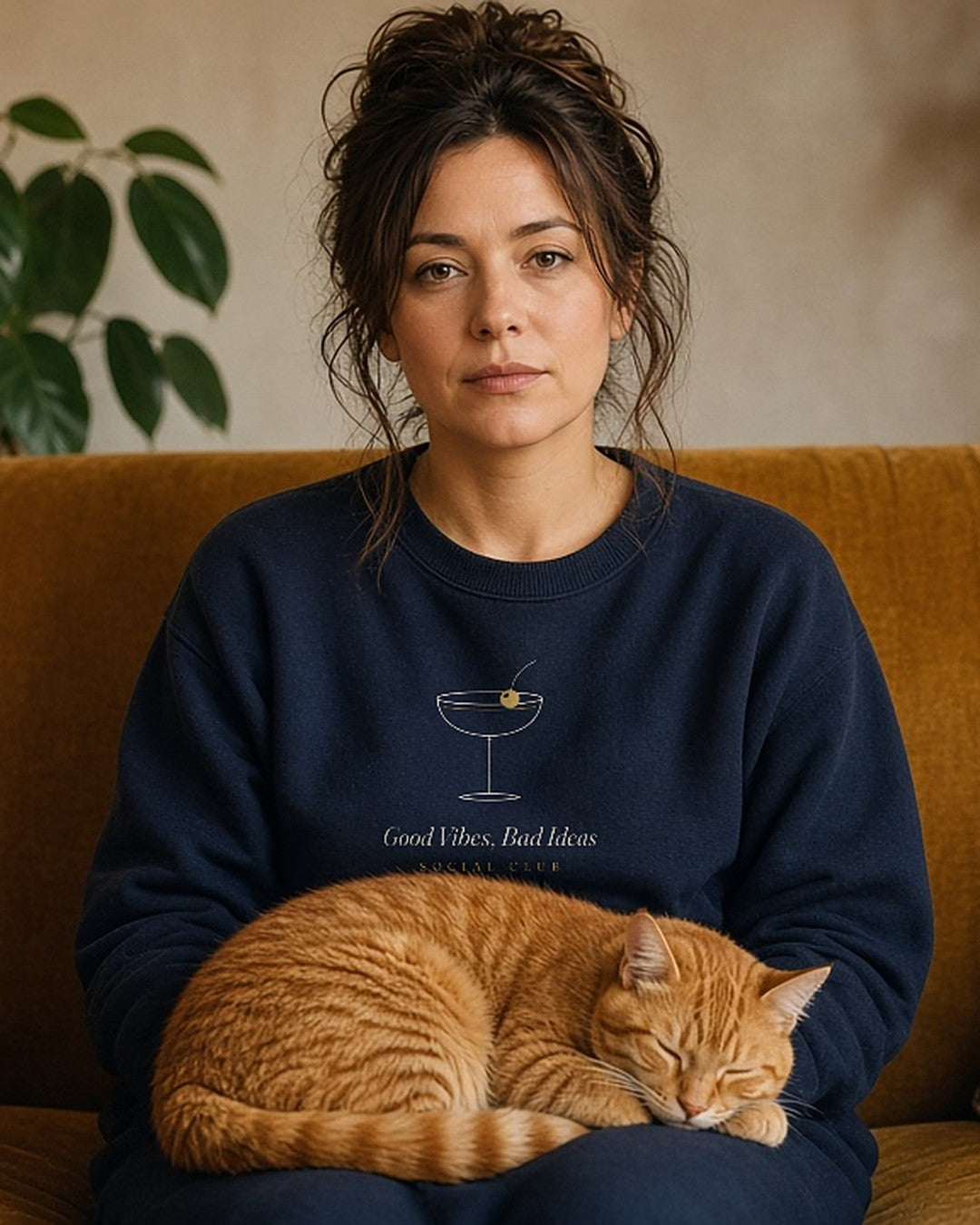 The Social Club Crewneck in Navy, on a mustard sofa with a ginger cat on her lap