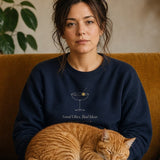 The Social Club Crewneck in Navy, on a mustard sofa with a ginger cat on her lap
