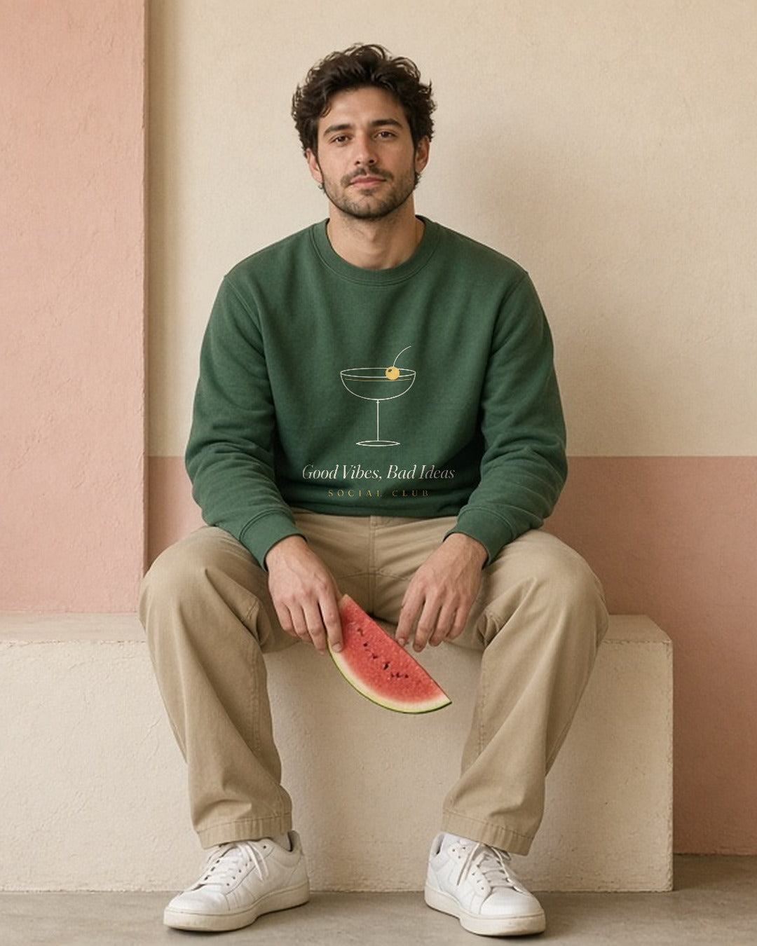 The Social Club Crewneck in Forest Green, sitting on a stucco ledge with a slice of watermelon