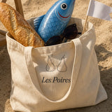 The Les Poires Tote in the sand by a striped beach chair, with a baguette and an inflatable fish
