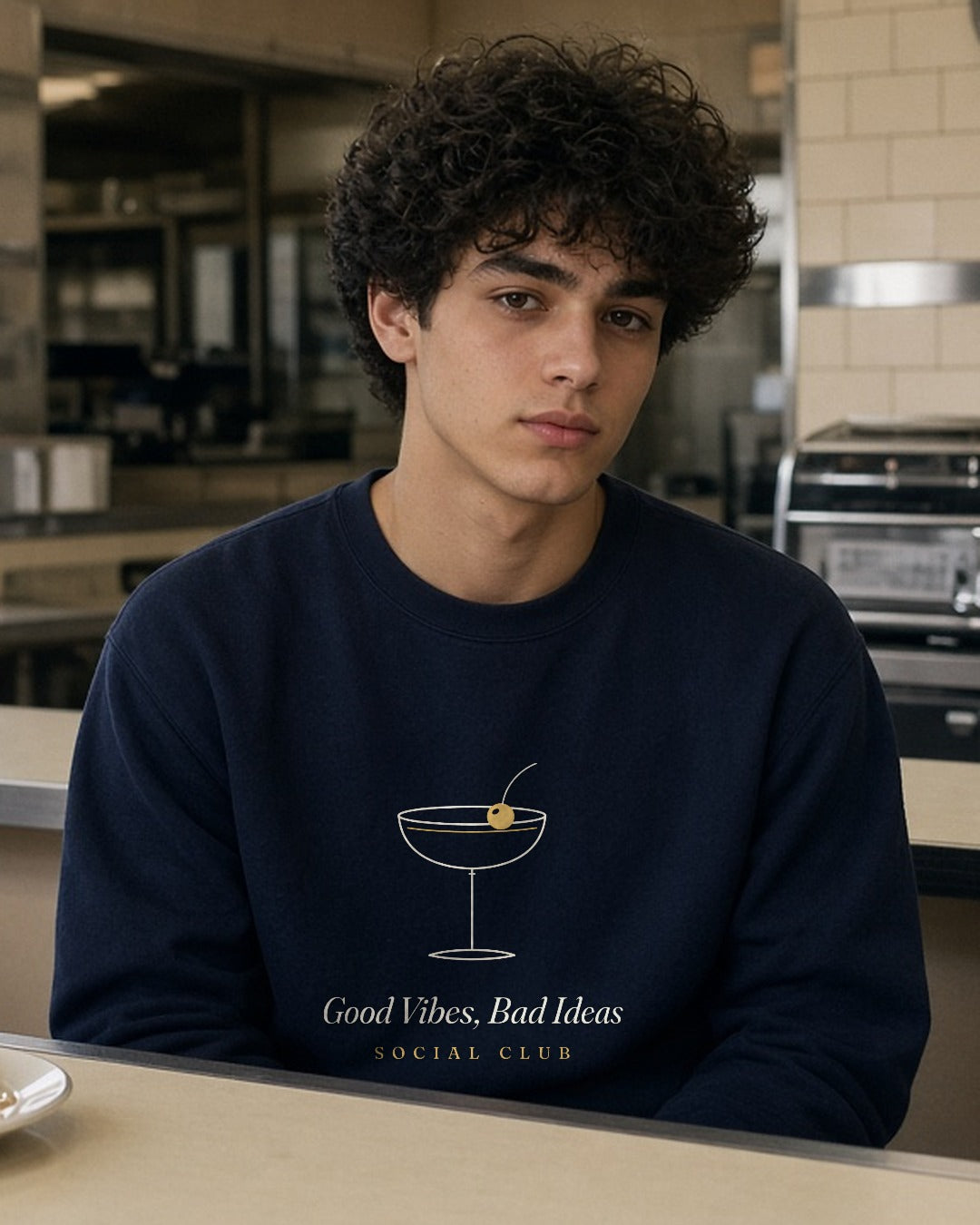 The Social Club Crewneck in Navy, at a diner counter with a slice of cake