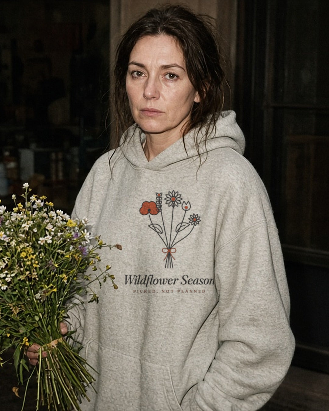 The Wildflower Season Hoodie in Oatmeal Heather, holding a wildflower bouquet at night