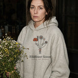 The Wildflower Season Hoodie in Oatmeal Heather, holding a wildflower bouquet at night