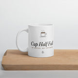The Cup Half Full Mug in White, styled on a table