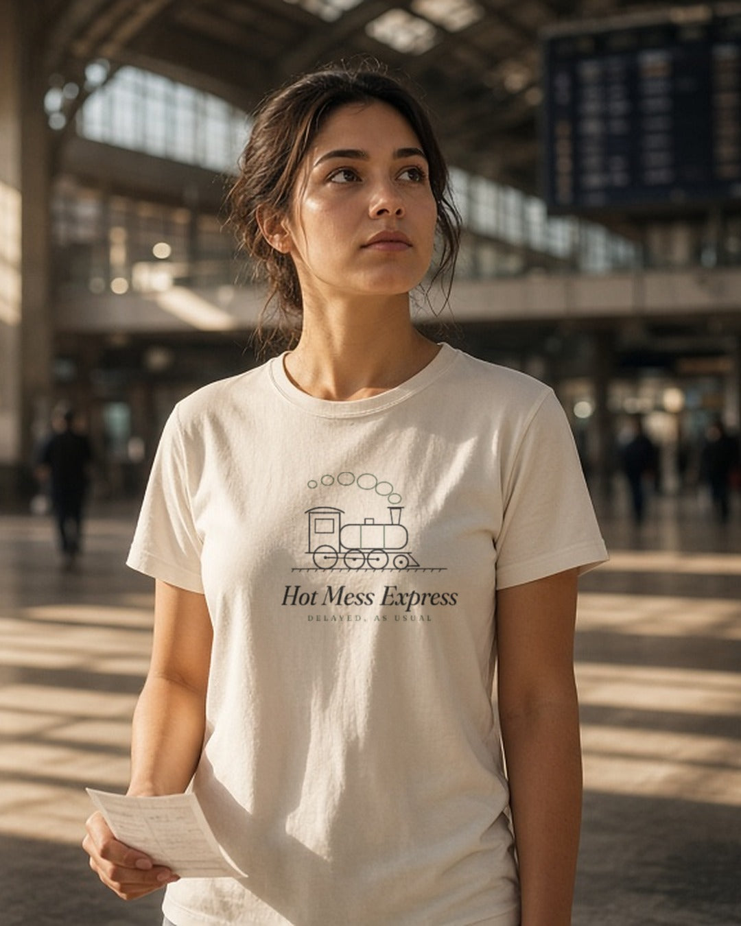 The Hot Mess Express Tee in Ivory, a woman (20s) in Ivory staring up at a departures board where every train says DELAYED