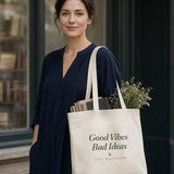 The House Tote in Oyster, oyster tote on a woman's shoulder outside a bookstore window, books and greens sticking out