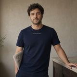 The House Tee in True Navy, same-type man at a café counter, small wordmark on chest, newspaper under his arm