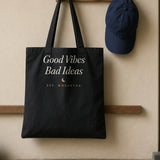 The House Tote in Black, black tote hanging on a peg by the front door beside a navy cap, shoes below