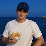 The Night Swim Dad Hat in Navy, worn at a boardwalk railing at blue hour with a boat of fries