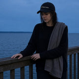 The Night Swim Dad Hat in Black, young woman with wet hair and a towel over her shoulder leaning on a pier rail at dusk