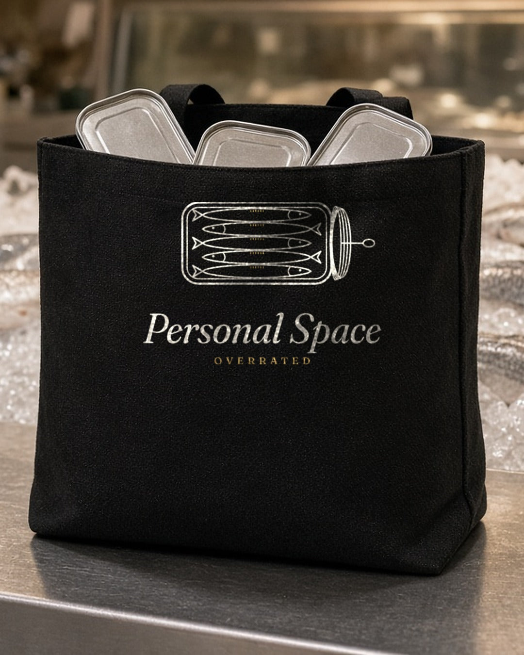 The Personal Space Tote in Black, the Black tote at a fish counter with a few sardine tins inside