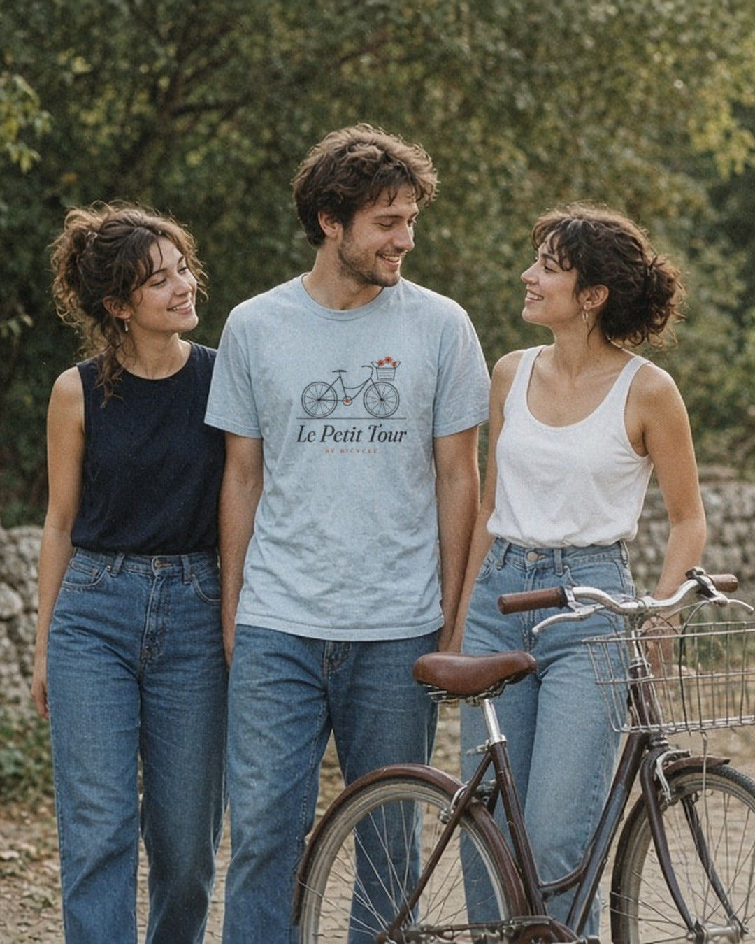 Le Petit Tour Tee in Chambray, man in the centre between two women on a country lane by a stone wall, vintage bike in front
