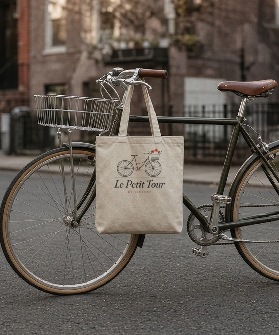 Le Petit Tour Tote in Oyster, tote hanging flat from the handlebar of a vintage bike on a brownstone street