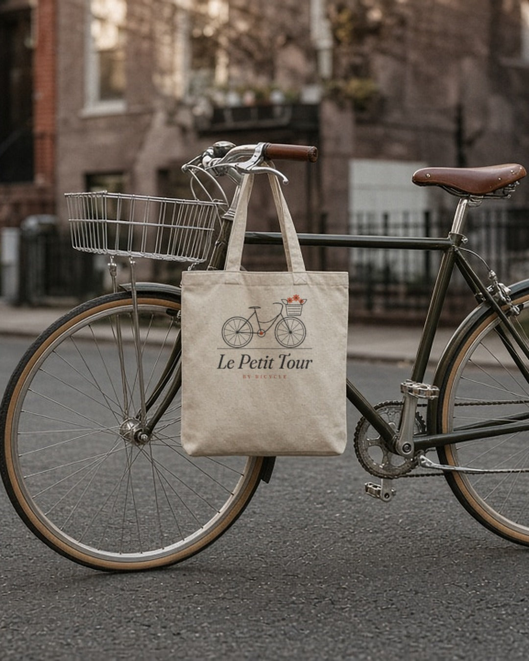 Le Petit Tour Tote in Oyster, tote hanging flat from the handlebar of a vintage bike on a brownstone street