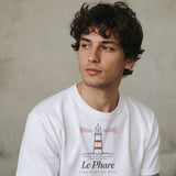 Le Phare Tee in White, close portrait of a young man in a white tee against a pale concrete wall, looking off to the side