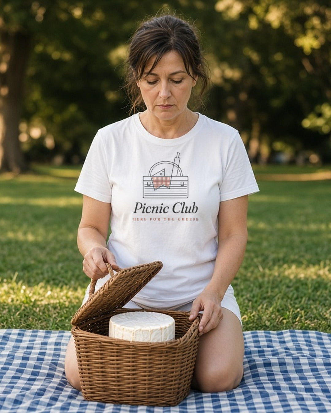 The Picnic Club Tee in White, a woman (40s) in White slowly lifting the basket lid to find one ant on the brie