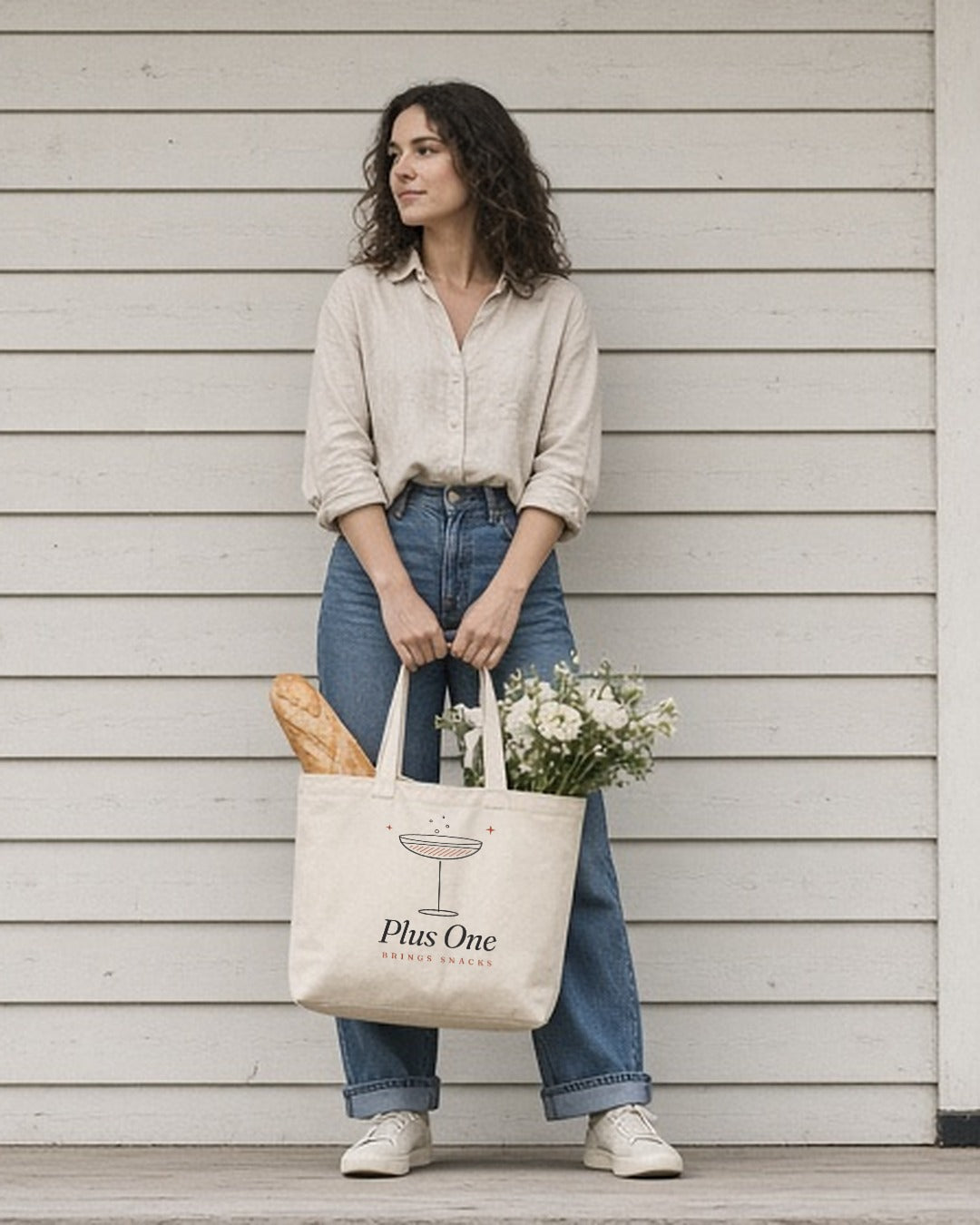 The Plus One Tote in Oyster, woman on a porch holding the tote with a baguette and flowers in front of her