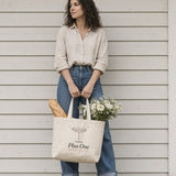 The Plus One Tote in Oyster, woman on a porch holding the tote with a baguette and flowers in front of her