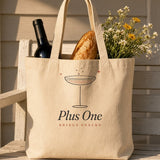 The Plus One Tote in Oyster, tote on a porch packed with a bottle of wine, a baguette and wildflowers